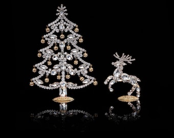 May include: A sparkling, crystal-encrusted Christmas tree ornament and a reindeer ornament, both with gold accents, on a black background.
