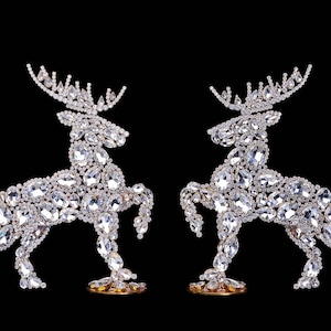 May include: Two silver reindeer figurines made of rhinestones, standing on gold bases against a black background.