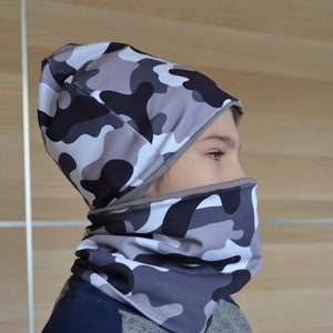 May include: A gray and black camouflage beanie and neck gaiter set. The beanie has a fold-over brim and the neck gaiter is a tube shape.