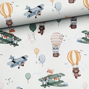 May include: A white fabric with a repeating pattern of airplanes, hot air balloons, animals, and clouds. The airplanes are blue and green, the hot air balloons are orange, yellow, and brown, the animals are foxes, raccoons, bears, and rabbits, and the clouds are white.