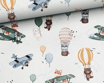 May include: A white fabric with a repeating pattern of airplanes, hot air balloons, animals, and clouds. The airplanes are blue and green, the hot air balloons are orange, yellow, and brown, the animals are foxes, raccoons, bears, and rabbits, and the clouds are white.