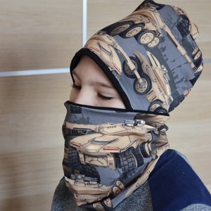 May include: A gray and black knit hat and neck warmer with a pattern of beige military vehicles. The hat has a fold-over brim and the neck warmer is a tube shape.