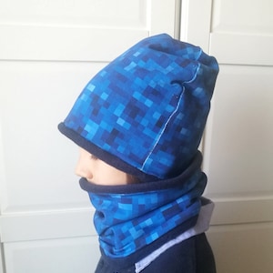 May include: A blue and black pixelated beanie and neck warmer set. The beanie has a fold-over cuff and the neck warmer is a loop style.
