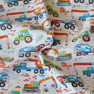 May include: A white fabric with a repeating pattern of colorful construction vehicles. The vehicles include a crane, a tractor, a cement mixer, and an excavator. The fabric has a white background with orange, blue, green, and yellow accents.