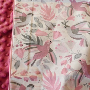 Pode incluir: Um cobertor para beb&eacute; rosa e branco com um padr&atilde;o de p&aacute;ssaros e flores. O cobertor tem uma textura macia e felpuda de um lado e uma textura lisa de algod&atilde;o do outro lado.
