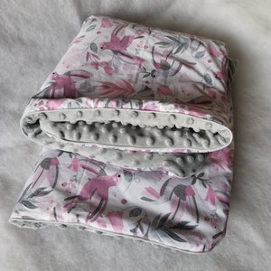 Pode incluir: Um cobertor macio para beb&eacute;, de cor cinzento e branco, com um padr&atilde;o floral rosa e p&aacute;ssaros. O cobertor &eacute; revers&iacute;vel com um lado cinzento que tem uma superf&iacute;cie texturizada e irregular.