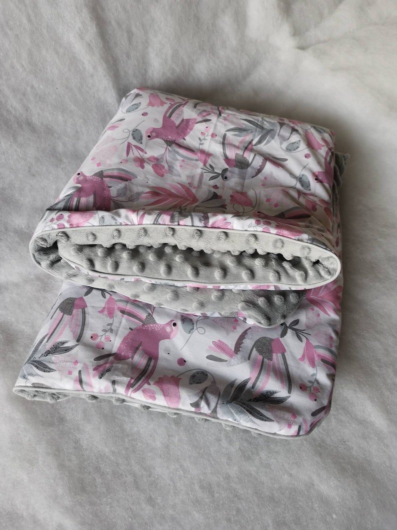 Pode incluir: Um cobertor macio para beb&eacute;, de cor cinzento e branco, com um padr&atilde;o floral rosa e p&aacute;ssaros. O cobertor &eacute; revers&iacute;vel com um lado cinzento que tem uma superf&iacute;cie texturizada e irregular.