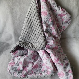 Pode incluir: Um cobertor para beb&eacute; cinzento e rosa com um lado macio e texturizado e um lado estampado com p&aacute;ssaros cor-de-rosa e folhas.