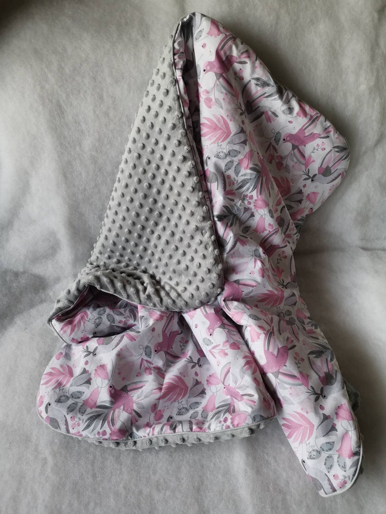 Pode incluir: Um cobertor para beb&eacute; cinzento e rosa com um lado macio e texturizado e um lado estampado com p&aacute;ssaros cor-de-rosa e folhas.