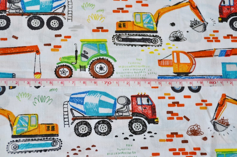 May include: A white fabric with a repeating pattern of colorful construction vehicles. The vehicles include a cement mixer, a tractor, an excavator, and a crane. The fabric also features brick patterns and green grass.