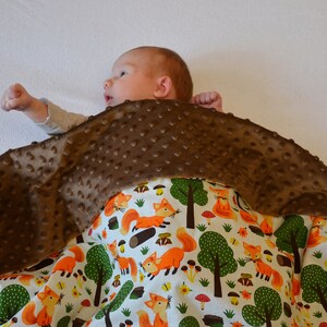 May include: A brown and white baby blanket with a fox print. The blanket is made of soft, plush fabric and is perfect for cuddling.
