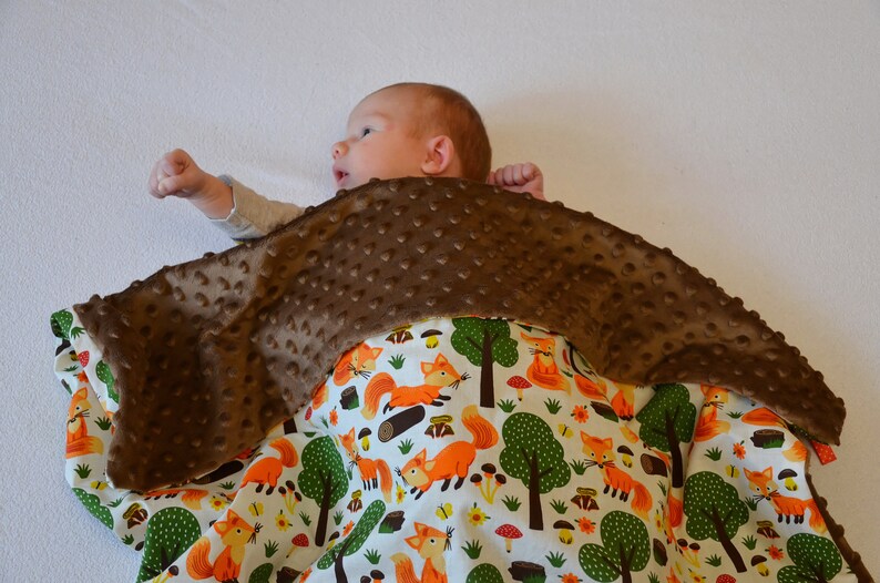 May include: A brown and white baby blanket with a fox print. The blanket is made of soft, plush fabric and is perfect for cuddling.