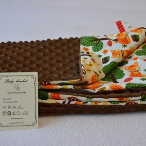 May include: A brown and white baby blanket with a fox print. The blanket is made of soft, plush fabric and has a textured surface. The blanket is folded in half and has a small tag attached to it that says "Baby blanket".