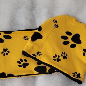 May include: A yellow knit hat and matching scarf with a black paw print pattern.