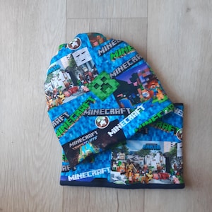 May include: A blue and green Minecraft-themed beanie hat with a black brim. The hat features a variety of Minecraft characters and logos, including Creeper, Steve, and the Minecraft logo.