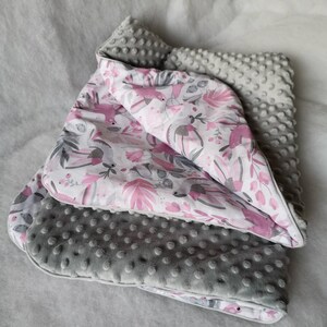 Pode incluir: Um cobertor para beb&eacute; cinzento e branco com um padr&atilde;o floral rosa e tecido texturizado cinzento. O cobertor est&aacute; dobrado ao meio e tem um toque macio e felpudo.