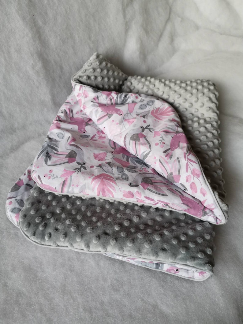 Pode incluir: Um cobertor para beb&eacute; cinzento e branco com um padr&atilde;o floral rosa e tecido texturizado cinzento. O cobertor est&aacute; dobrado ao meio e tem um toque macio e felpudo.