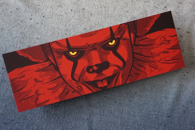 May include: A close-up of a red and black illustration of a clown with yellow eyes. The clown's mouth is open and shows teeth. The background is dark red.