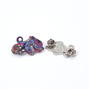 May include: Two octopus-shaped enamel pins. One pin is colorful with pink, purple, blue, and brown details. The other pin is silver with a detailed design. Both pins have a pin back.