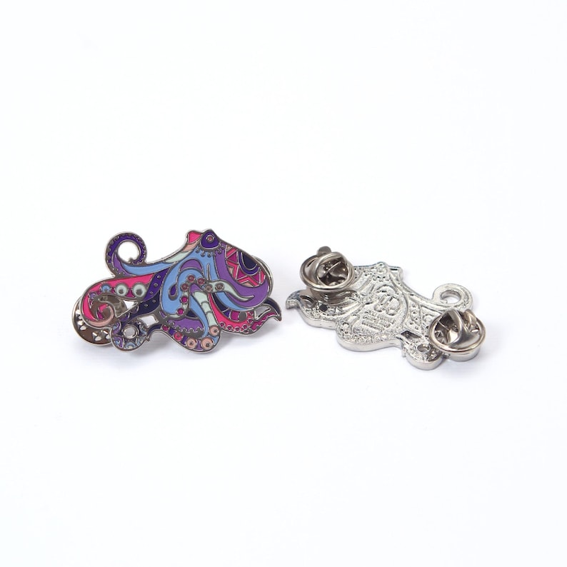 May include: Two octopus-shaped enamel pins. One pin is colorful with pink, purple, blue, and brown details. The other pin is silver with a detailed design. Both pins have a pin back.
