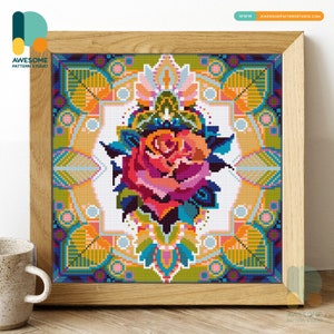 May include: A colorful cross-stitch pattern featuring a large pink rose with green leaves and a geometric border. The border is made up of various shapes and colors, including blue, yellow, orange, and green.