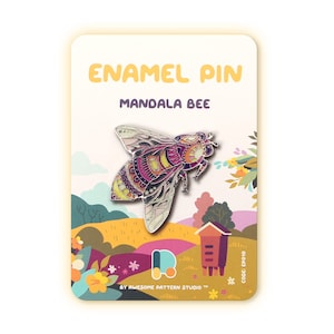 May include: Enamel pin featuring a detailed mandala bee design. The pin has a colorful, intricate pattern in shades of pink, yellow, and purple. The pin is on a card with the text "ENAMEL PIN MANDALA BEE" and a landscape illustration.