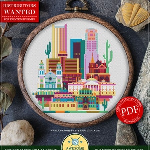 May include: Counted cross stitch pattern for instant download, titled "C603: Phoenix". The pattern depicts a colorful cityscape with skyscrapers, cacti, and a desert landscape. The pattern is 116 x 123 stitches and requires 18 colors of DMC thread.