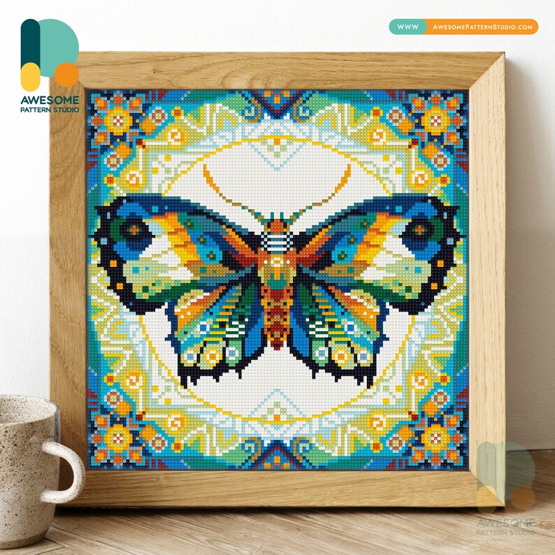 May include: A framed cross-stitch artwork featuring a vibrant butterfly design. The butterfly has blue, orange, green, and yellow wings, set against a white background with a geometric border. The frame is made of light-colored wood. The artwork is from Awesome Pattern Studio.
