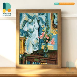 Puede incluir: Una obra de arte en punto de cruz enmarcada que presenta un busto blanco de una figura clásica. La obra de arte incluye un jarrón con flores y está ambientada sobre un fondo azul y amarillo. El marco es de madera y la obra se exhibe sobre una superficie de madera.