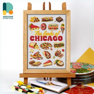 May include: A framed cross-stitch sampler on a wooden easel, featuring various Chicago foods. The text "The foods of CHICAGO" is prominently displayed. The sampler includes images of pizza, sandwiches, and other local delicacies.