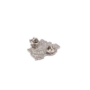 May include: A silver-colored pin shaped like a map of a country, with two pin backs. The pin has a detailed, textured surface and is set against a white background. The pin is likely a collectible or souvenir.