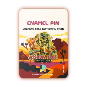May include: Enamel pin featuring a colorful illustration of Joshua Tree National Park, with a Joshua Tree, a desert tortoise, a coyote, and a bird. The pin is gold-toned with a pink and yellow background. The text "Joshua Tree National Park" is printed on the card.