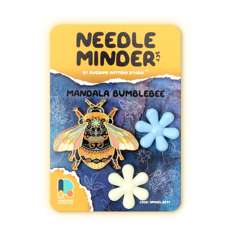 May include: A "Needle Minder Set" featuring a mandala bumblebee design. The set includes a decorative bumblebee pin with gold, black, pink, and blue accents, along with two flower-shaped magnets. The card has the text "Awesome Pattern Studio".