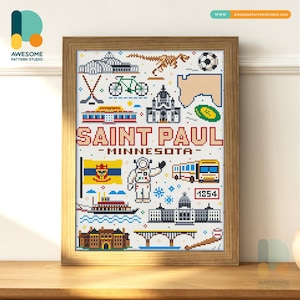 May include: A framed cross-stitch artwork depicting Saint Paul, Minnesota, with various icons. The design includes a flag, astronaut, bus, and buildings, all in a pixelated style. The wooden frame surrounds the artwork, which is a colourful piece.