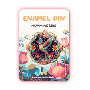 Puede incluir: Pin esmaltado con diseño de colibrí. El pin tiene un fondo azul oscuro con detalles florales y de colibrí coloridos. El texto "ENAMEL PIN HUMMINGBIRD" se muestra en la parte superior. El pin está sobre una tarjeta blanca con ilustraciones florales.