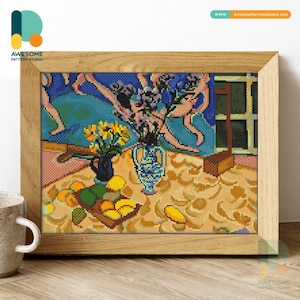 Puede incluir: Un punto de cruz enmarcado de un bodegón con flores y frutas. La obra presenta un fondo azul con figuras, un mantel amarillo y un marco de madera. La imagen incluye un jarrón azul con flores amarillas y un jarrón azul y blanco con flores moradas.