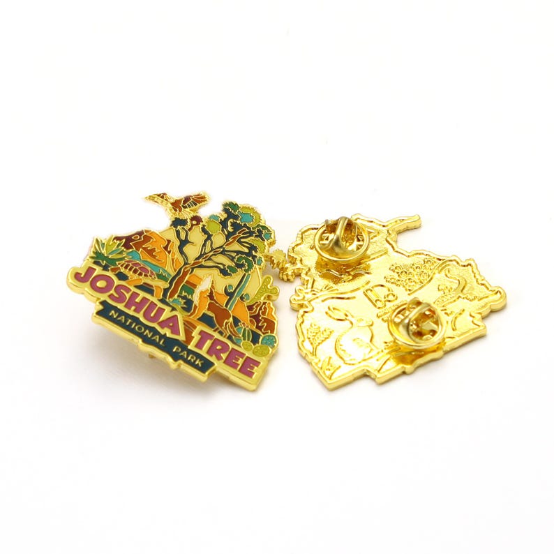 May include: Gold-colored metal pin with a colorful image of Joshua Tree National Park. The pin features a Joshua Tree, a desert landscape, and the words "Joshua Tree National Park".