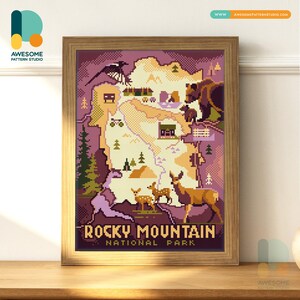 May include: A framed print depicting a pixelated map of Rocky Mountain National Park. The artwork includes illustrations of wildlife, trees, and a magpie. The text "ROCKY MOUNTAIN NATIONAL PARK" is displayed at the bottom in a brown font.