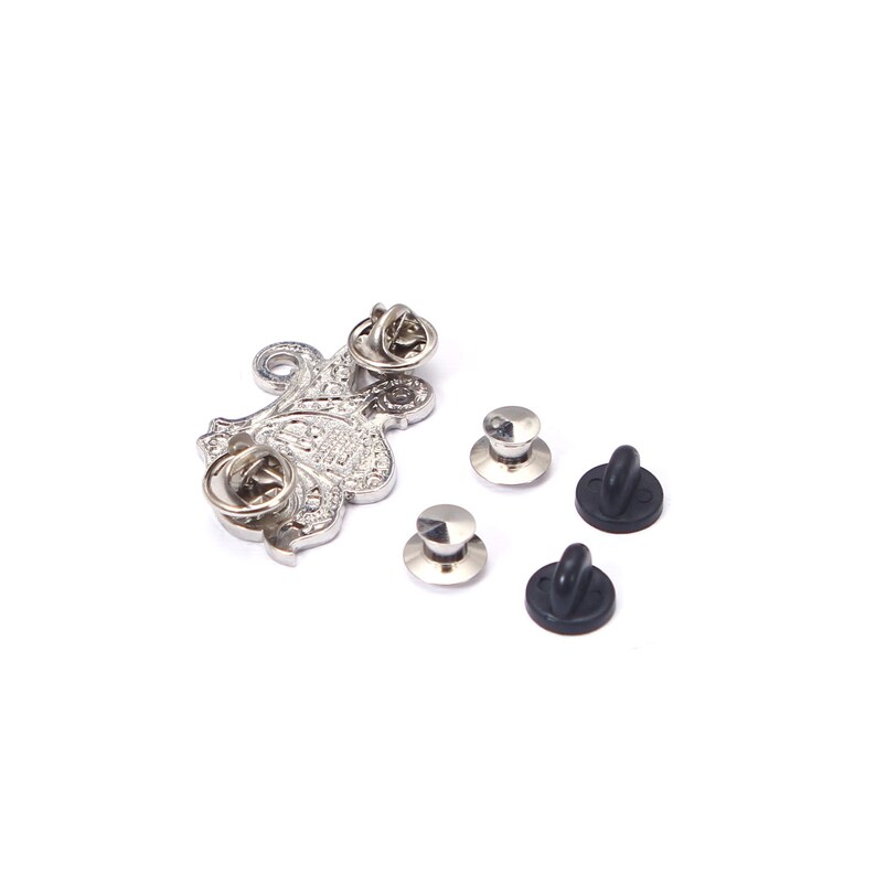 May include: A silver-colored metal pin with an ornate floral design, along with several pin backs. The pin has a textured surface and a classic aesthetic. The pin backs are silver and black.