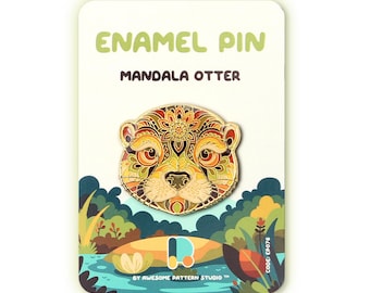 May include: Enamel pin with a mandala otter design in gold, orange, and brown hues. The pin is presented on a card with the text "ENAMEL PIN MANDALA OTTER" and a nature-themed backdrop depicting a river and foliage.