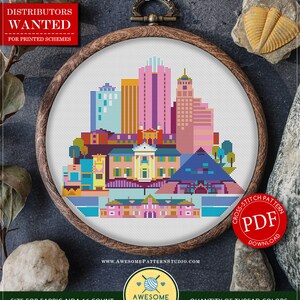 May include: A colorful cross-stitch pattern of the Memphis skyline, displayed in a wooden embroidery hoop. The design features buildings in shades of pink, blue, yellow, and orange. The text "COUNTED CROSS STITCH PATTERN" and "Memphis" are visible. The pattern size is 8.69 x 7.56 inches.