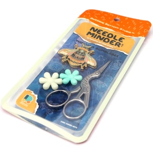 May include: A packaged needle minder set featuring a decorative bumblebee pin, flower-shaped stitch markers, and crane-shaped embroidery scissors. The package includes the text "NEEDLE MINDER" and "MANDALA BUMBLEBEE".