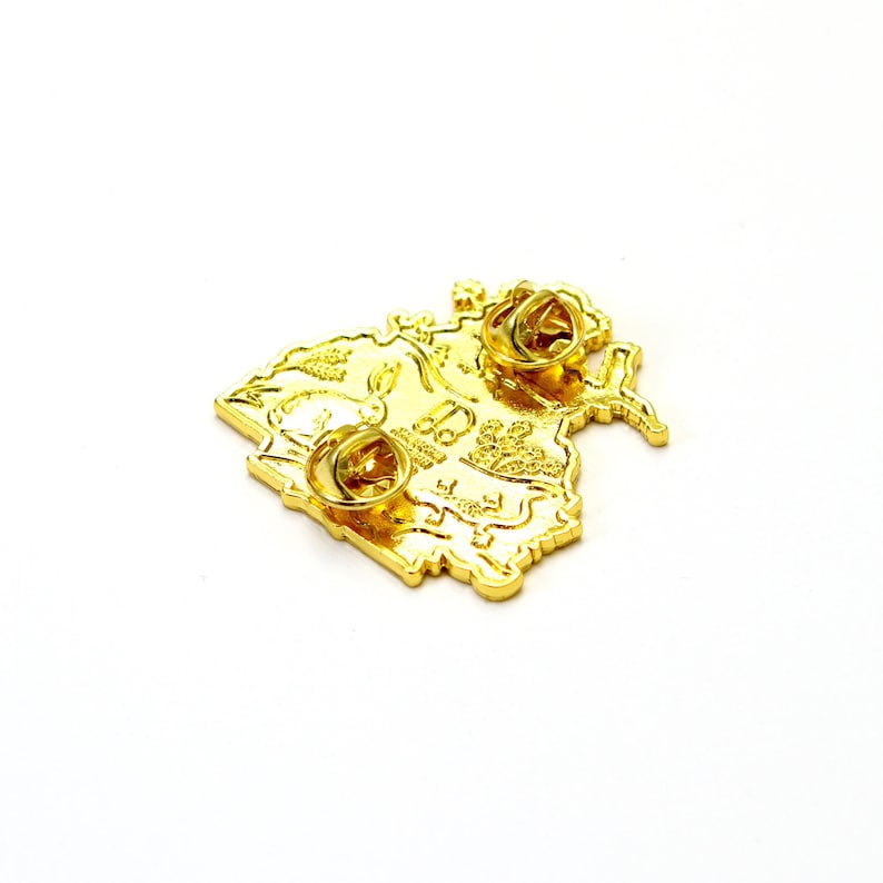 May include: Gold-colored metal pin with a detailed design of a map. The pin has a butterfly shape and features a textured surface. The back of the pin has two metal clasps.