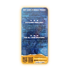May include: A rectangular needle minder with a blue and yellow floral design. The text on the card reads "Not Just a Needle Minder" and "Stitching Made Easy". The card also mentions scissors and embroidery kits.
