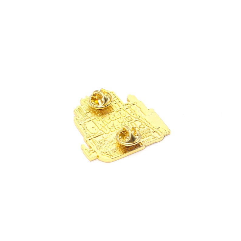 May include: A gold-colored pin featuring a detailed map of Chicago, USA. The pin has two gold-colored pin backs. The text "Chicago USA" is visible on the pin.