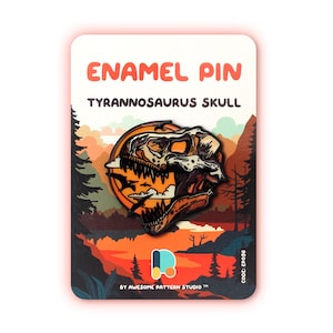 May include: Enamel pin featuring a Tyrannosaurus skull design. The pin is set against a backdrop of a sunset landscape with trees and mountains. The text "ENAMEL PIN" and "TYRANNOSAURUS SKULL" are displayed in orange. The pin is on a card with the text "BY AWESOME PATTERN STUDIO".