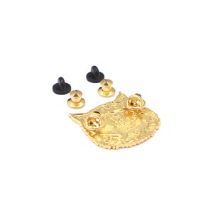 Puede incluir: Un pin de metal dorado con forma de cara de gato, con dos cierres de alfiler adjuntos. Tambi&eacute;n se incluyen dos cierres de alfiler de goma negra adicionales y dos cierres de alfiler dorados. El pin tiene detalles intrincados.