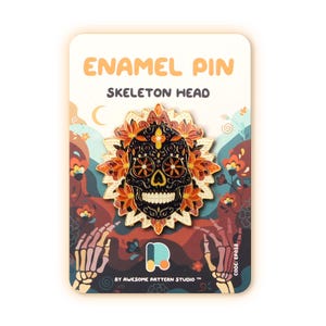 May include: Enamel pin featuring a black skeleton head adorned with orange and yellow flowers. The pin is on a card with the text "ENAMEL PIN SKELETON HEAD" and a floral background. The pin is from Awesome Pattern Studio.