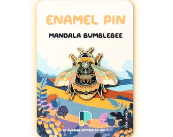 May include: An enamel pin with a mandala bumblebee design. The pin features a detailed, colourful pattern with gold accents. The pin is displayed on a card with the text "ENAMEL PIN MANDALA BUMBLEBEE". The card has a landscape illustration with flowers and mountains.
