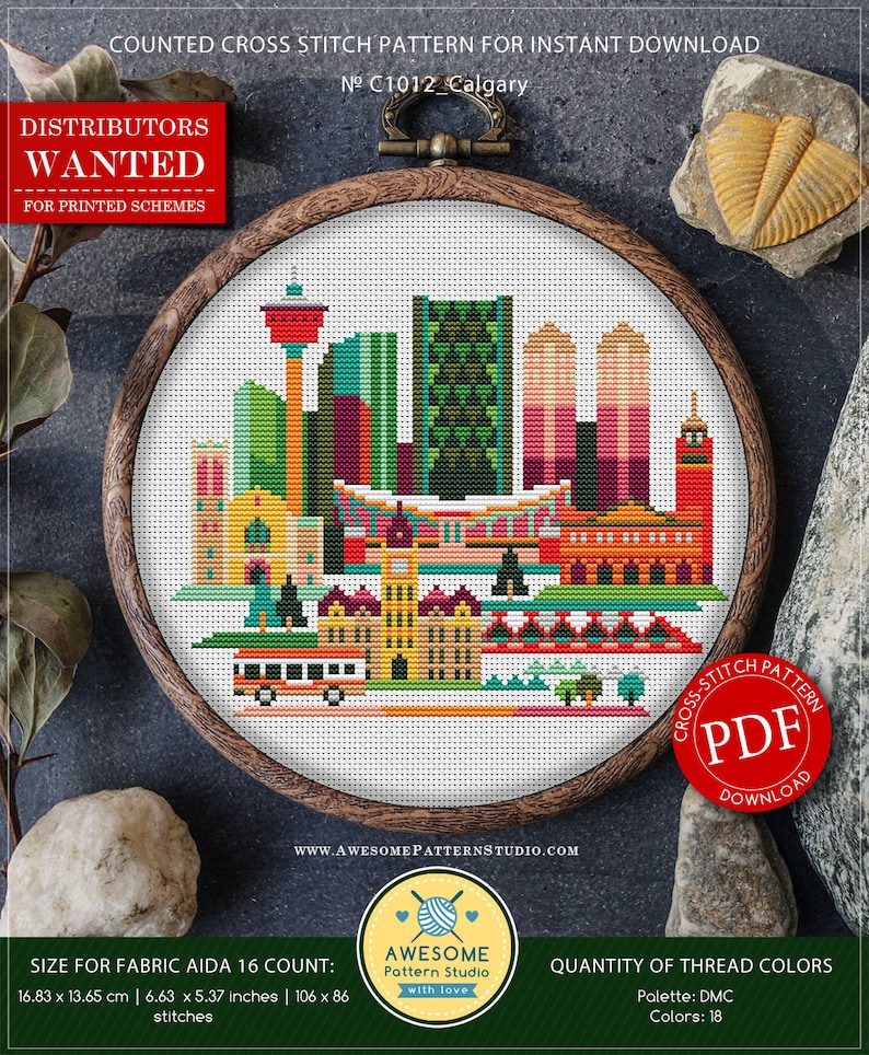 Op de afbeelding: Een geteld kruissteekpatroon voor Calgary, Canada, met een kleurrijke stadsgezicht met gebouwen, bruggen en een bus. Het patroon bevindt zich in een houten borduurring en is beschikbaar als PDF-download. Het patroon is 106 steken breed en 86 steken hoog en gebruikt 18 DMC-kleuren.